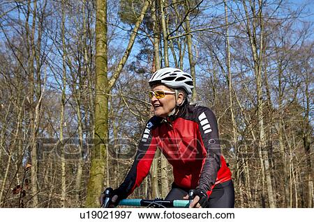 Stock Photo - Woman wearing cycling helmet and sunglasses cycling, looking away smiling. Fotosearch