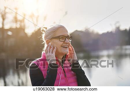 Stock Photo - Woman wearing glasses and earbuds, hands on ears looking away smiling. Fotosearch