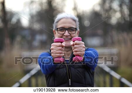 Stock Photo - Woman wearing glasses holding pink dumbbells looking at camera smiling. Fotosearch