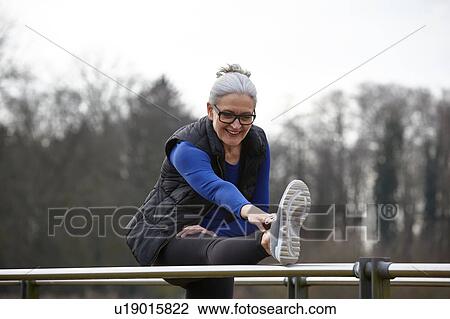 Woman with leg raised on railing bending forward stretching View Large Photo Image Stock Image - Woman with leg raised on railing bending forward stretching. Fotosearch