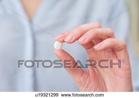 Stock Photo - Womans hand holding pill between thumb and forefinger. Fotosearch