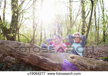 Stock Photo - Women in forest hands behind head doing sit up against fallen tree. Fotosearch