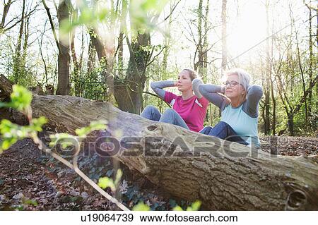 Stock Photo - Women in forest hands behind head doing sit up against fallen tree. Fotosearch