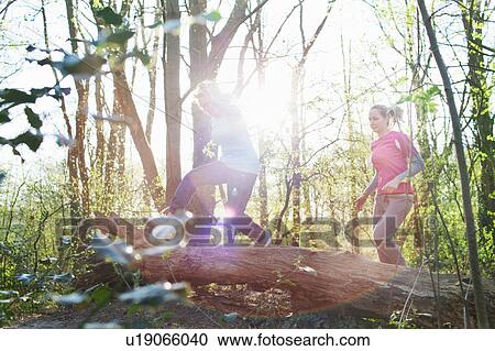 Stock Image - Women in forest jumping over fallen tree. Fotosearch