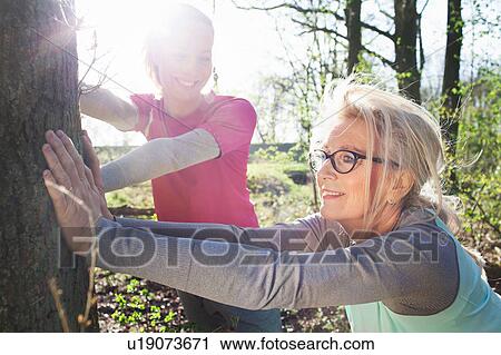 Stock Image - Women in forest leaning against tree stretching. Fotosearch