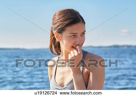 Picture - Women in front of ocean with finger in mouth looking away. Fotosearch