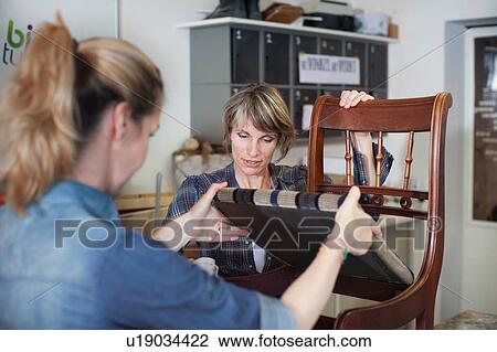 Stock Image - Women in workshop examining chair. Fotosearch