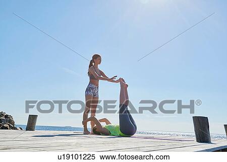 Stock Photography - Women on pier holding each others ankles exercising. Fotosearch