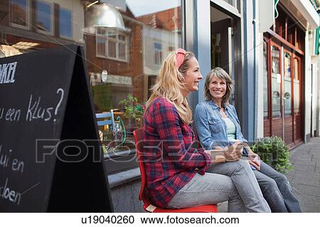 Women sitting on chairs in front of shop holding coffee cups smiling View Large Photo Image Stock Image - Women sitting on chairs in front of shop holding coffee cups smiling. Fotosearch