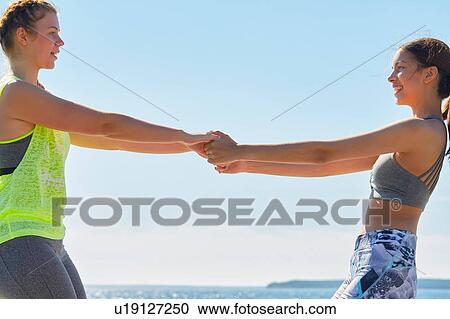Stock Image - Women wearing sports clothes face to face holding hands smiling. Fotosearch