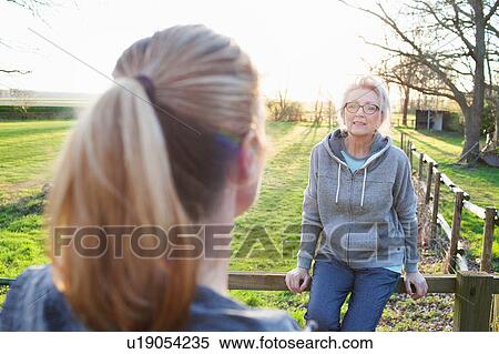 Women wearing sports clothing leaning against fence talking to friend View Large Photo Image Stock Photography - Women wearing sports clothing leaning against fence talking to friend. Fotosearch