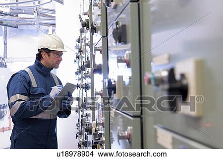 Picture - Worker inspecting switch gear in hydroelectric power station. Fotosearch
