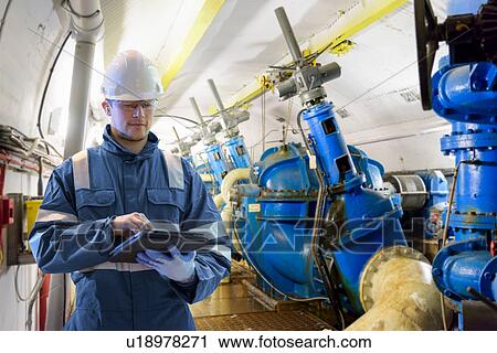 Stock Image - Worker using digital tablet to take readings in straining gallery in hydroelectric power station. Fotosearch