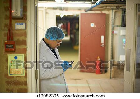 Worker wearing hair and latex gloves leaning against doorway using smartphone View Large Photo Image Stock Photography - Worker wearing hair and latex gloves leaning against doorway using smartphone. Fotosearch