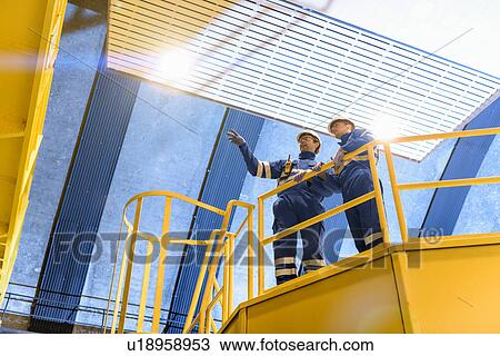 Stock Image - Workers in generating hall in hydroelectric power station, low angle view. Fotosearch
