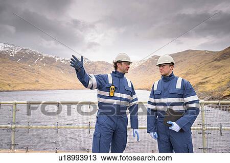 Stock Image - Workers on dam with water at hydroelectric power station. Fotosearch