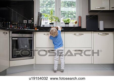 Stock Image - Young boy in kitchen, reaching up for freshly baked muffins, rear view. Fotosearch