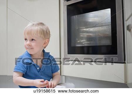 Stock Photography - Young boy sitting on floor in kitchen, beside oven. Fotosearch