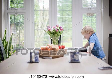 Young boy standing at table looking at digital tablet View Large Photo Image Stock Photo - Young boy standing at table looking at digital tablet. Fotosearch
