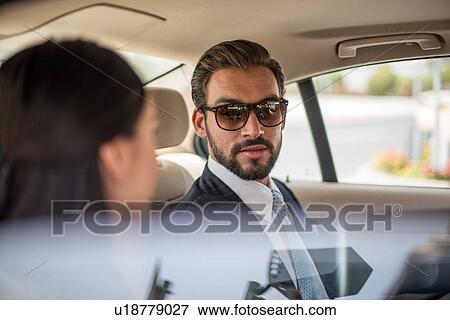 Stock Photo - Young businessman and woman talking in car backseat, Dubai, United Arab Emirates. Fotosearch