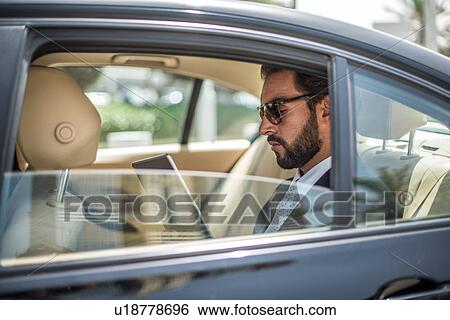 Stock Photograph - Young businessman using digital tablet in car backseat, Dubai, United Arab Emirates. Fotosearch