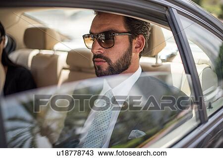 Stock Image - Young businessman wearing sunglasses in car backseat, Dubai, United Arab Emirates. Fotosearch