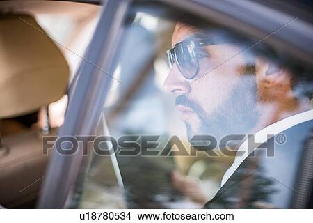Picture - Young businessman wearing sunglasses looking out of car window from backseat, Dubai, United Arab Emirates. Fotosearch