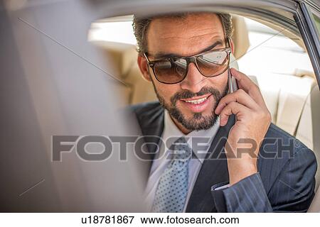 Young businessman wearing sunglasses talking on smartphone in car backseat, Dubai, United Arab Emirates View Large Photo Image Stock Photo - Young businessman wearing sunglasses talking on smartphone in car backseat, Dubai, United Arab Emirates. Fotosearch