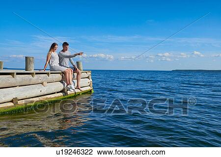 Young couple sitting on wooden pier, relaxing View Large Photo Image Stock Image - Young couple sitting on wooden pier, relaxing. Fotosearch
