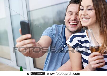 Young couple sitting outdoors, taking self portrait, using smartphone View Large Photo Image Stock Photography - Young couple sitting outdoors, taking self portrait, using smartphone. Fotosearch