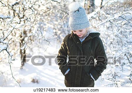Stock Image - Young girl in snowy landscape, hands in pockets, looking down. Fotosearch