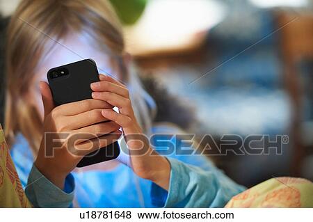 Stock Photo - Young girl looking at smartphone, face illuminated by glow of screen. Fotosearch