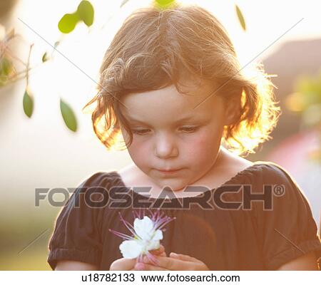 Stock Image - Young girl, outdoors, holding flower. Fotosearch