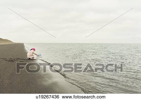 Stock Photograph - Young girl playing on beach at water's edge, Eyrarbakki, Iceland. Fotosearch