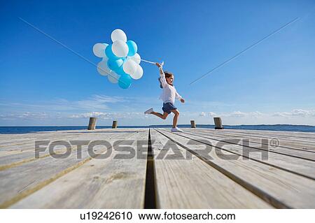 Young girl running on wooden pier, holding bunch of balloons View Large Photo Image Stock Image - Young girl running on wooden pier, holding bunch of balloons. Fotosearch