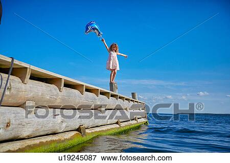 Young girl standing on wooden post on pier, holding helium balloon View Large Photo Image Stock Photo - Young girl standing on wooden post on pier, holding helium balloon. Fotosearch