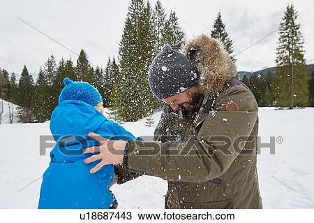 Stock Image - Young man and son having snowball fight in winter, Elmau, Bavaria, Germany. Fotosearch