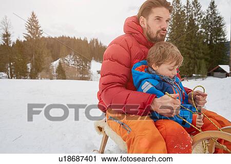 Stock Image - Young man and son tobogganing in snow, Elmau, Bavaria, Germany. Fotosearch