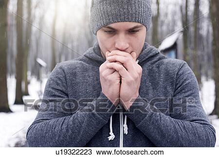 Stock Image - Young man breathing on hands, in snowy forest. Fotosearch