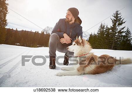 Young man crouching with husky in snow covered landscape, Elmau, Bavaria, Germany View Large Photo Image Stock Photo - Young man crouching with husky in snow covered landscape, Elmau, Bavaria, Germany. Fotosearch