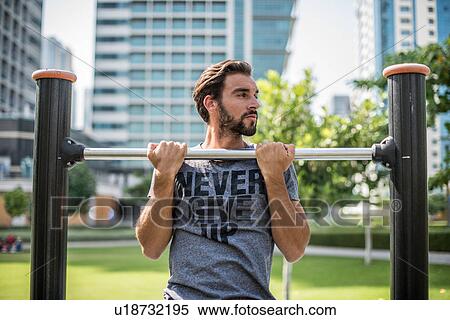 Stock Photography - Young man doing pull ups on park exercise equipment, Dubai, United Arab Emirates. Fotosearch