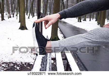 Stock Image - Young man exercising, stretching, in snowy forest, low section. Fotosearch