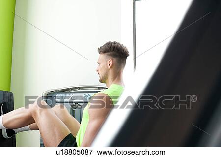 Stock Photo - Young man in gym using exercise equipment. Fotosearch