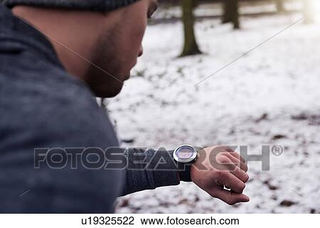 Young man in snowy forest, looking at watch, rear view View Large Photo Image Stock Image - Young man in snowy forest, looking at watch, rear view. Fotosearch