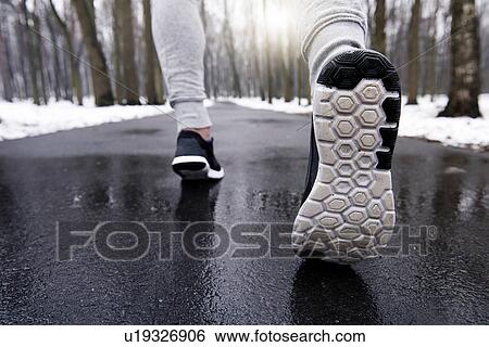 Stock Photograph - Young man jogging through snowy forest, low section, rear view. Fotosearch