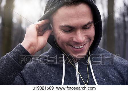 Young man outdoors, wearing hooded sweatshirt and earphones, smiling View Large Photo Image Stock Photo - Young man outdoors, wearing hooded sweatshirt and earphones, smiling. Fotosearch