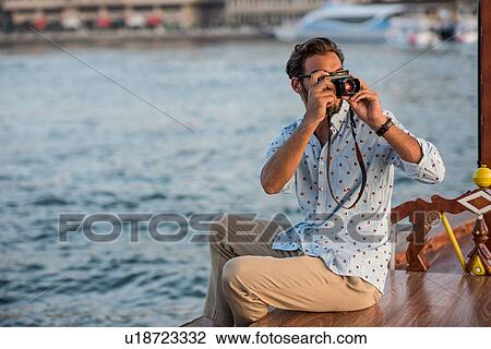 Stock Image - Young man photographing from boat at Dubai marina, United Arab Emirates. Fotosearch