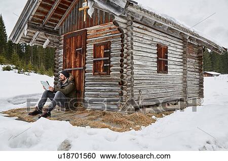 Young man reading map sitting outside log cabin in winter, Elmau, Bavaria, Germany View Large Photo Image Stock Image - Young man reading map sitting outside log cabin in winter, Elmau, Bavaria, Germany. Fotosearch