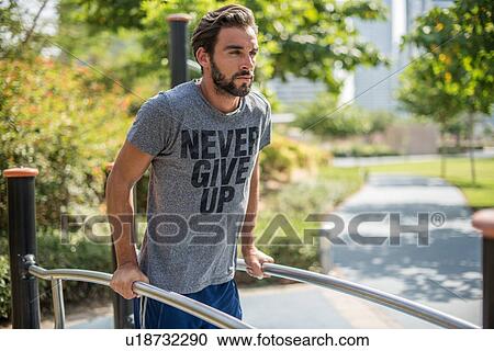 Stock Image - Young man training on exercise equipment in park, Dubai, United Arab Emirates. Fotosearch