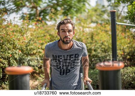 Stock Image - Young man training on park exercise equipment, Dubai, United Arab Emirates. Fotosearch